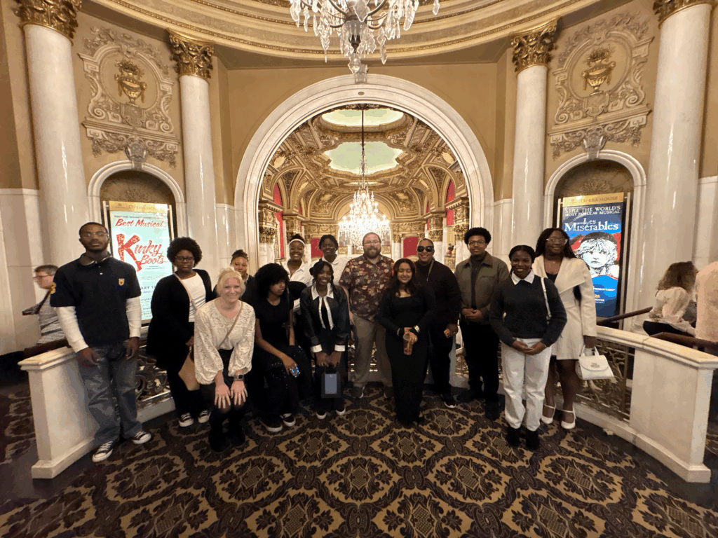 Students stand in the middle of the Boston Opera House surrounded by gold and silver adorned walls.
